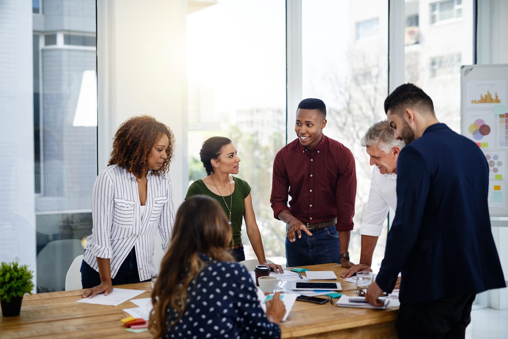 A high-resolution image depicting a diverse group of professional coaches collaborating in a modern workspace. They are engaged in discussion around a table with documents and laptops, symbolizing teamwork and coaching.