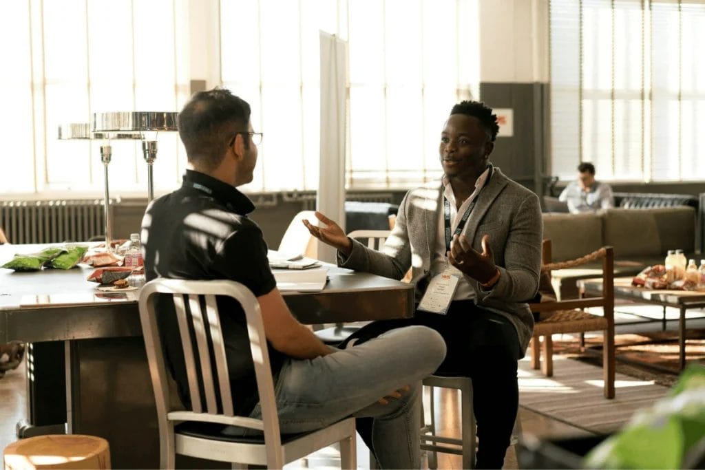 Two men having a discussion at a high table in a sunlit modern office setting.