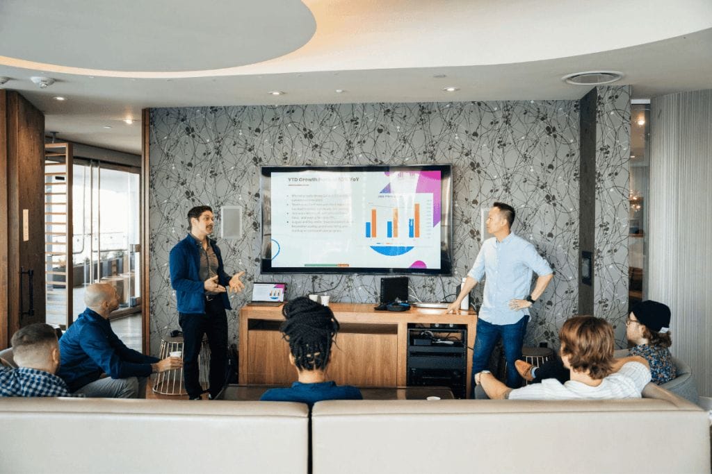Business team meeting with two men presenting a growth chart on a screen in a modern office.