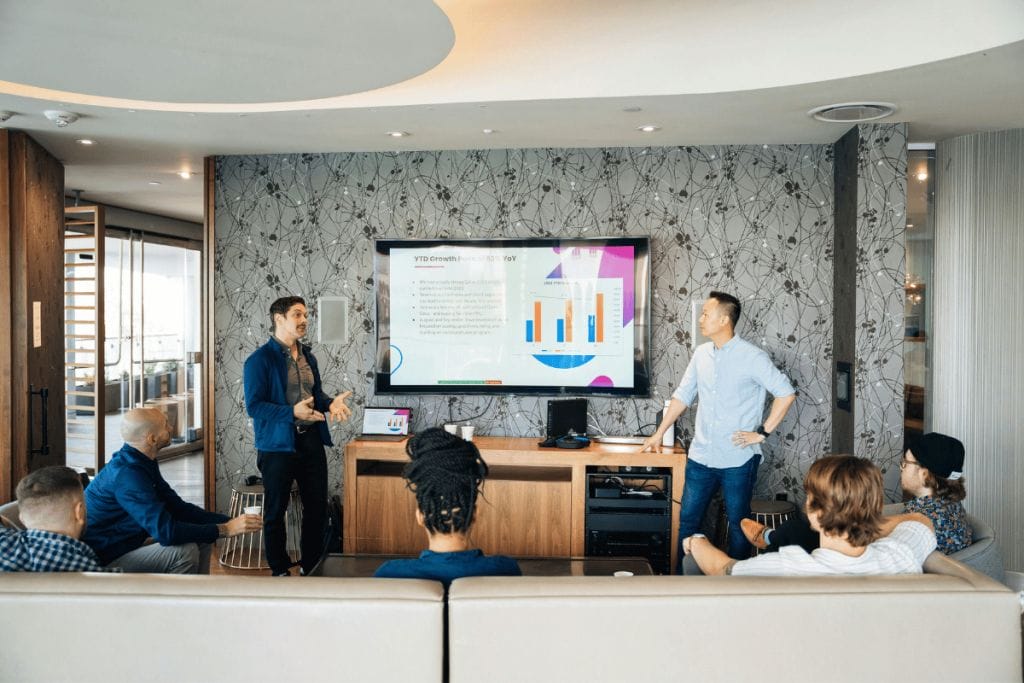 Business team meeting with two men presenting a growth chart on a screen in a modern office.