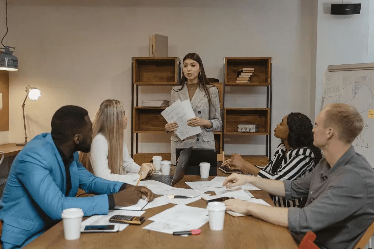 Business meeting with a woman presenting documents to colleagues around a table in a modern office setting.