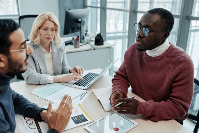 Three coworkers in a meeting, discussing documents in a modern office.