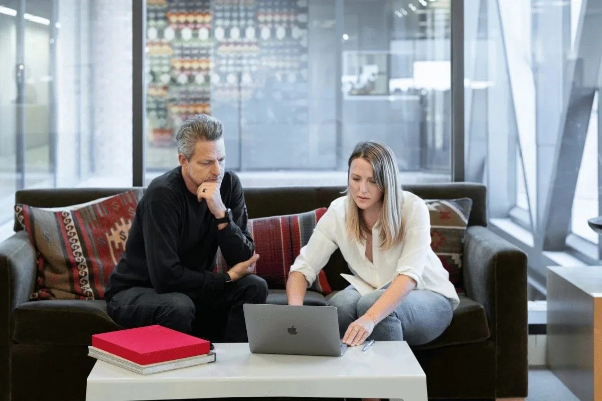 Two colleagues collaborating on a project using a laptop on a sofa.