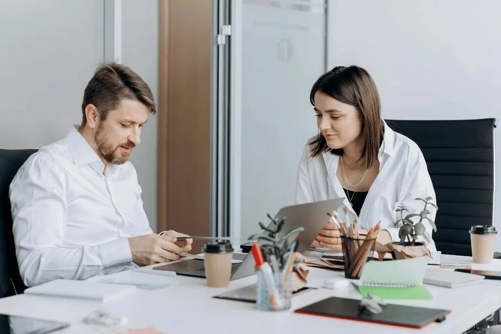 Man and woman in a discussion, surrounded by office supplies.