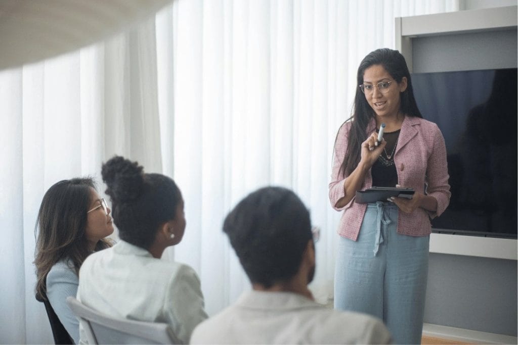 Woman presenting to a small group in a bright room.