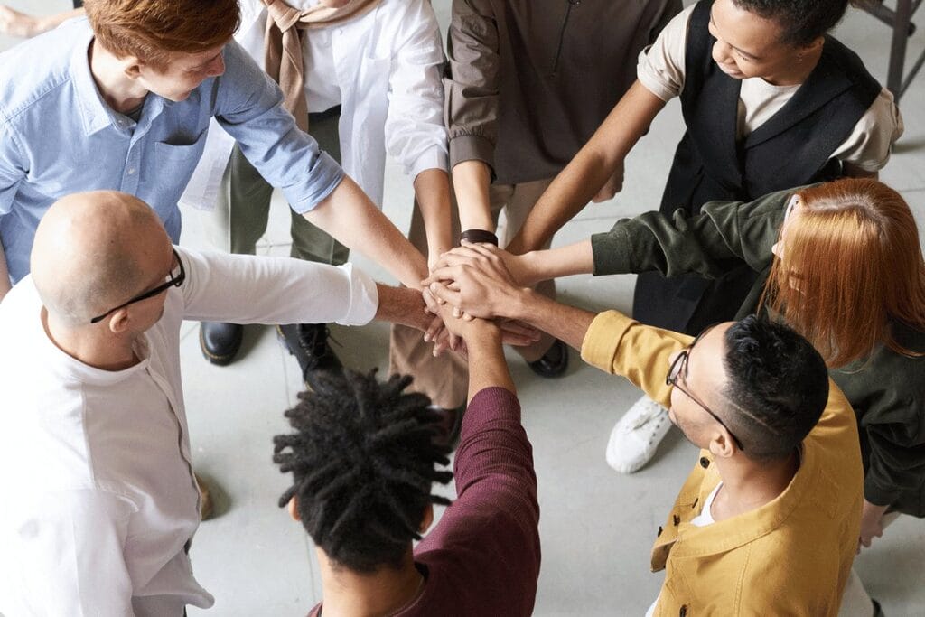 Diverse team members join hands in a high-five, showcasing teamwork in an office environment.