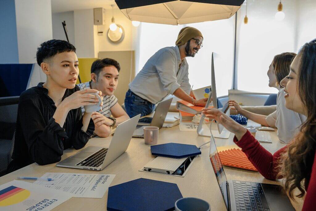 A diverse group of individuals collaborating around a table, each engaged with their laptops in a productive environment.