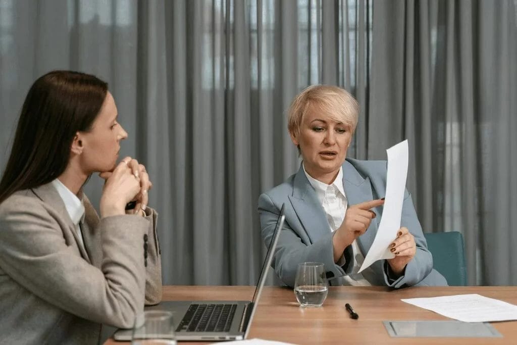 Two professional women engaged in a detailed conversation over a report.