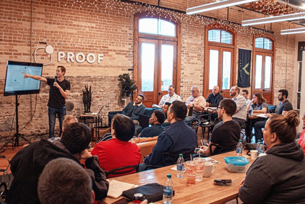 A diverse group of individuals seated at tables, engaged in conversation within a well-lit room.