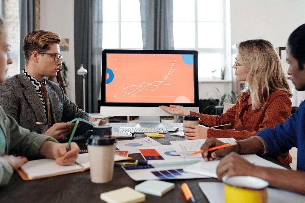 Colleagues analyzing a graph on a computer monitor in a collaborative workspace.