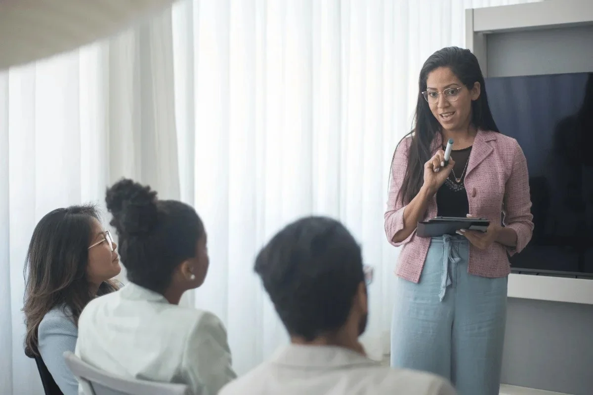 Woman leading a presentation with an attentive audience in a bright room.
