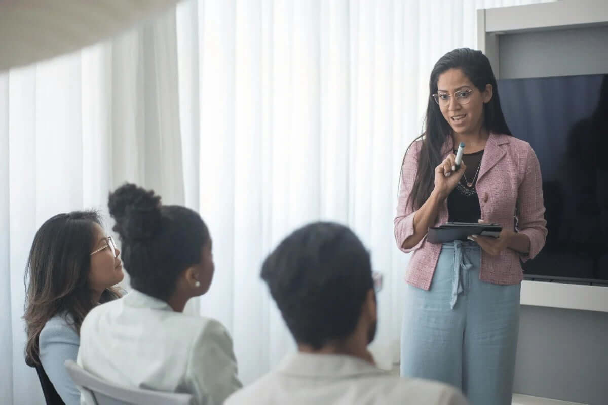 Woman leading a presentation with an attentive audience in a bright room.
