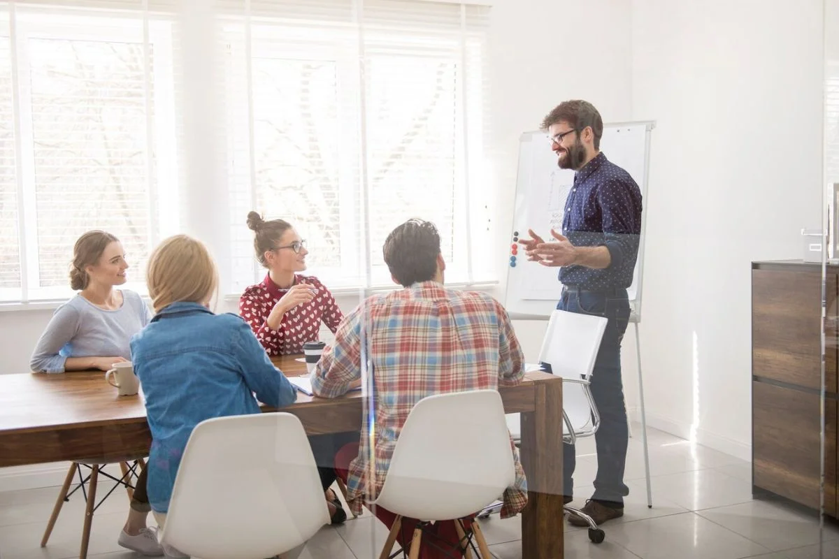 Team meeting in a bright office with a man presenting at a whiteboard.