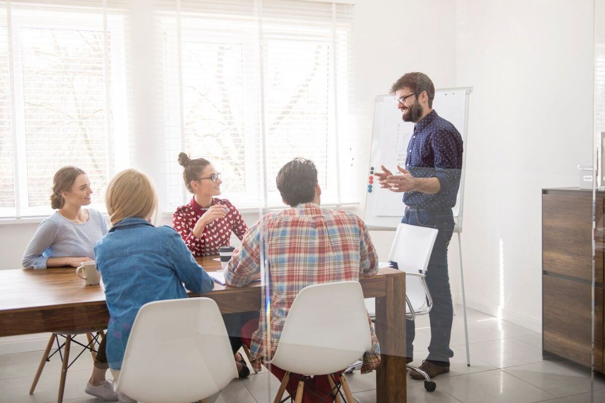 Team meeting in a bright office with a man presenting at a whiteboard.