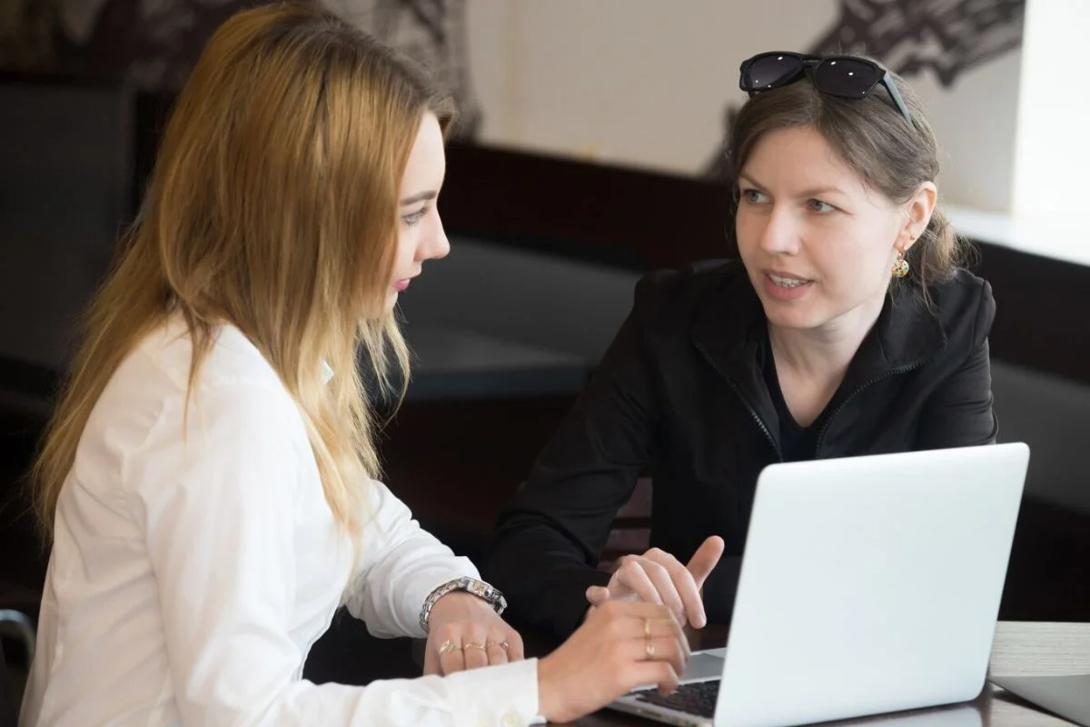 Two women discussing work on a laptop in a casual office setting.