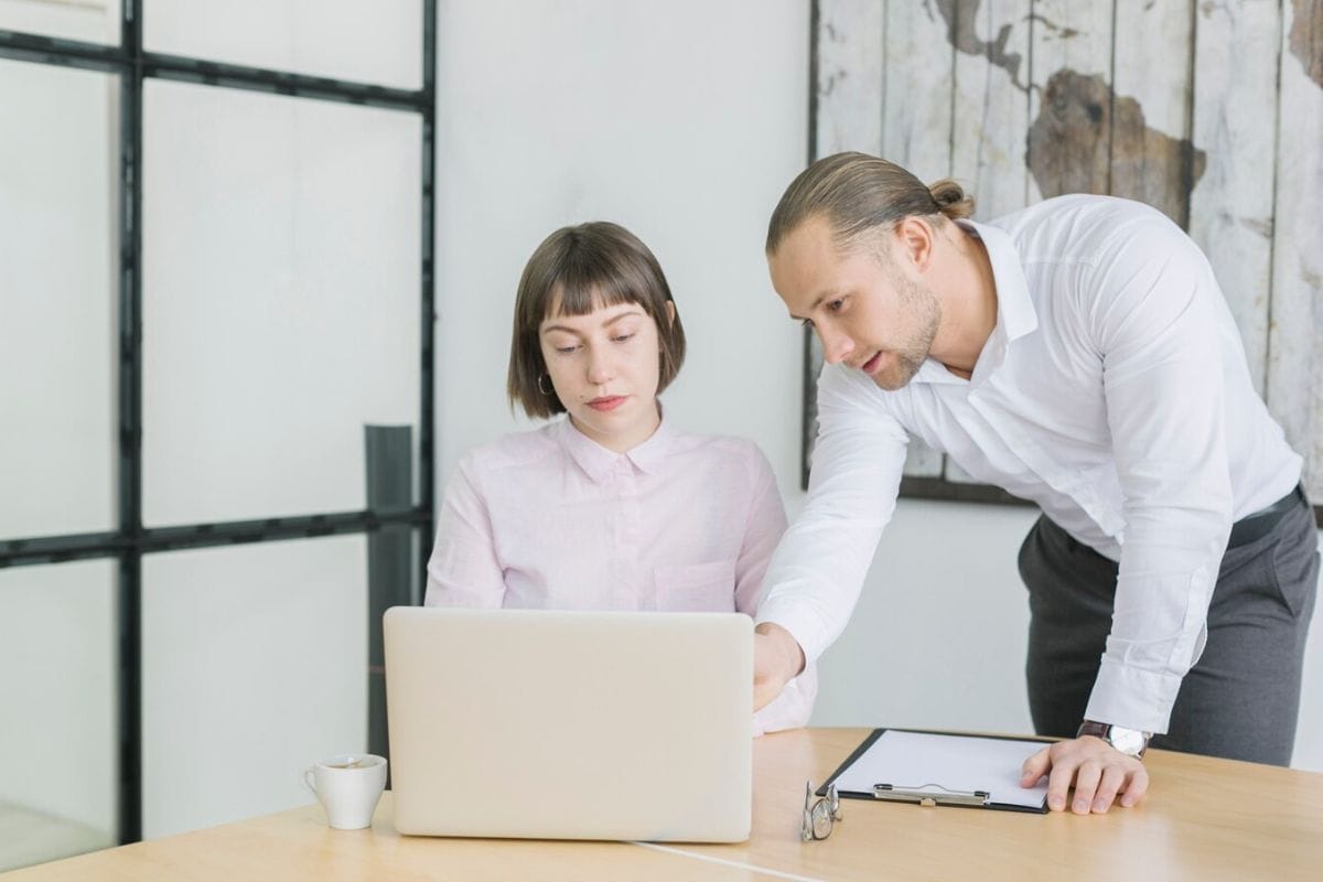 A man helping a woman with her laptop in a modern office setting.