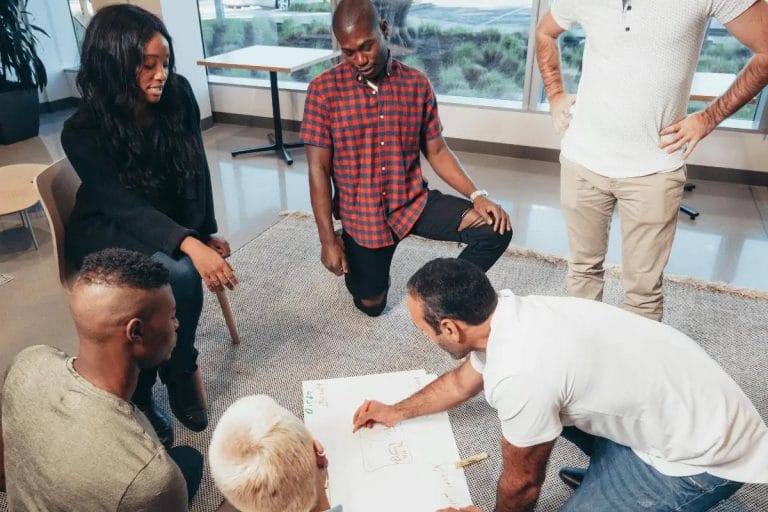 Team brainstorming session on the floor with a whiteboard in a modern office setting.