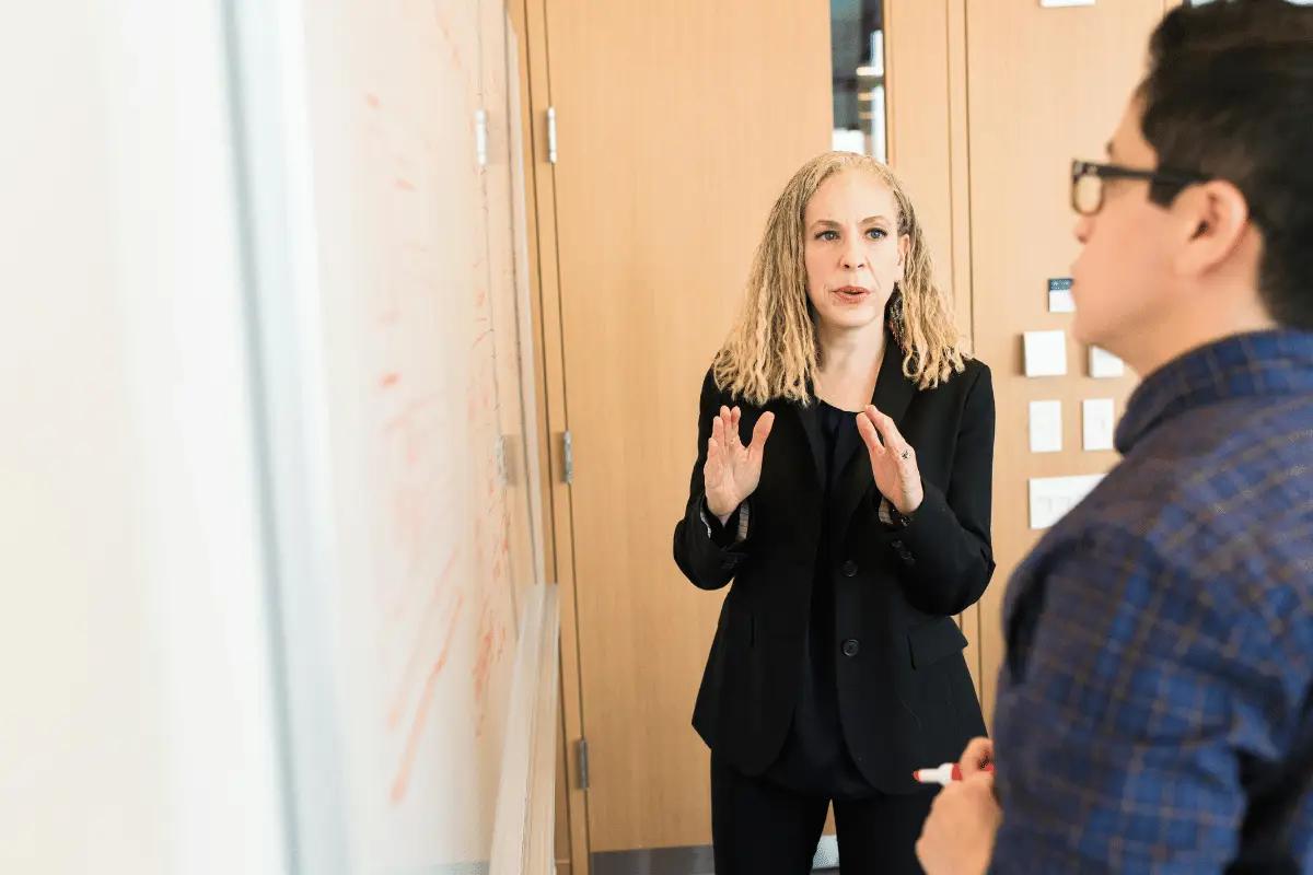 A businesswoman explaining a concept to a colleague during a whiteboard presentation in a modern office.