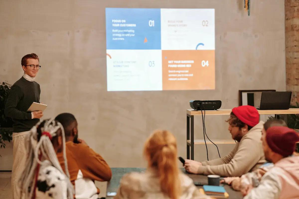 A presenter delivering a PowerPoint presentation to a small audience in a cozy, modern workspace.