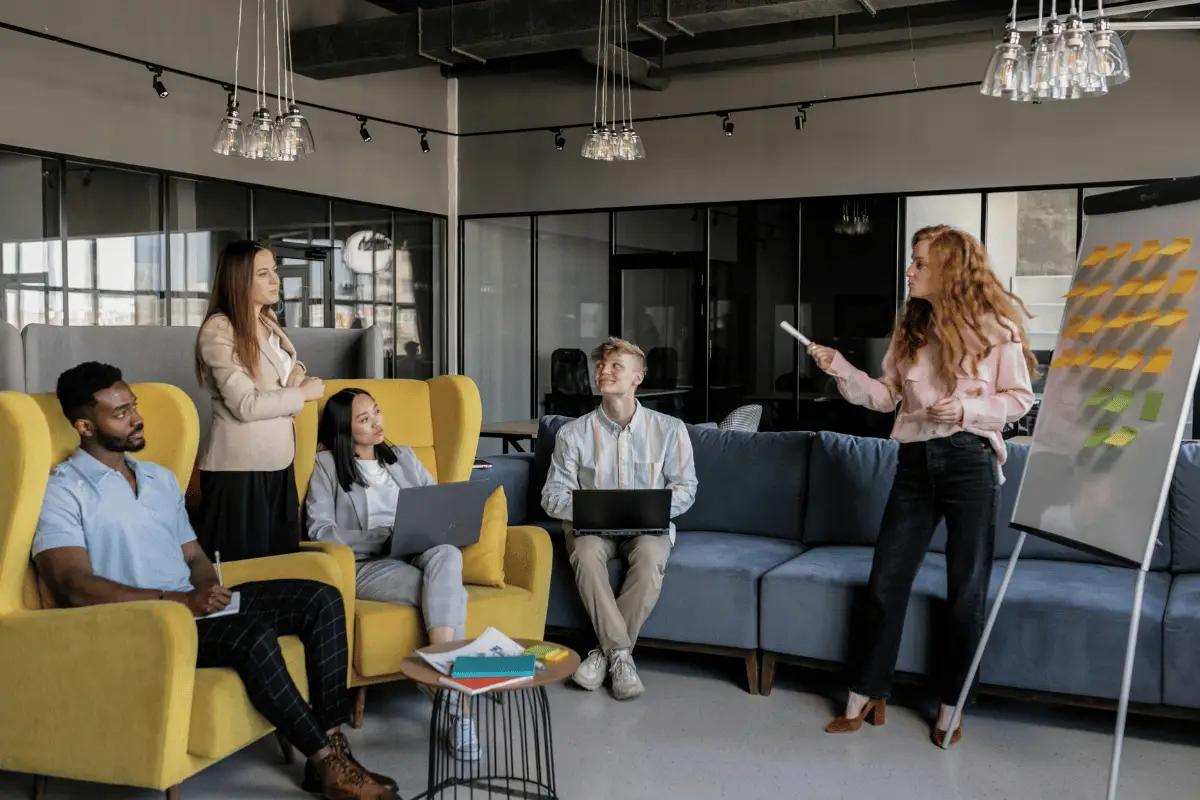 A team brainstorming session in a modern office with a presenter leading a discussion using sticky notes on a flip chart.