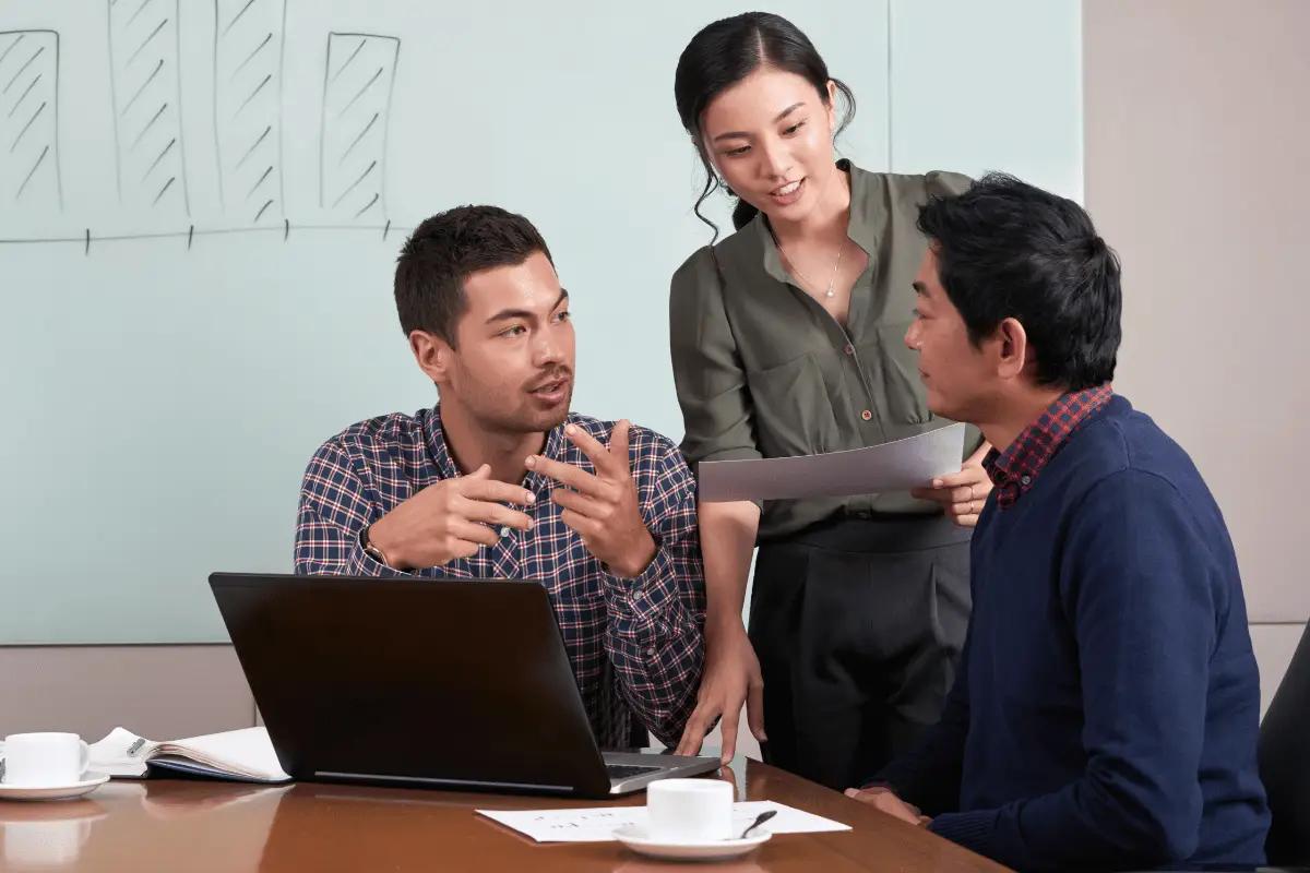 Three colleagues discussing ideas during a meeting, with one person explaining and pointing to a laptop screen.
