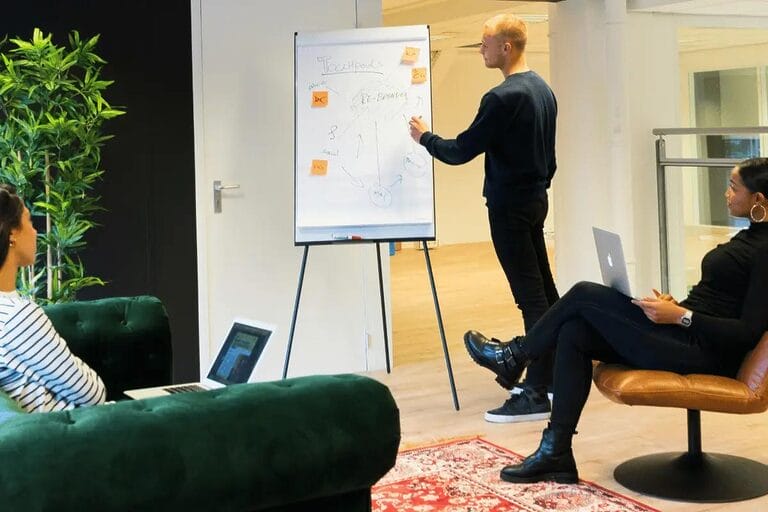 A group of individuals seated in office chairs, engaged in discussion near a whiteboard filled with notes and ideas.