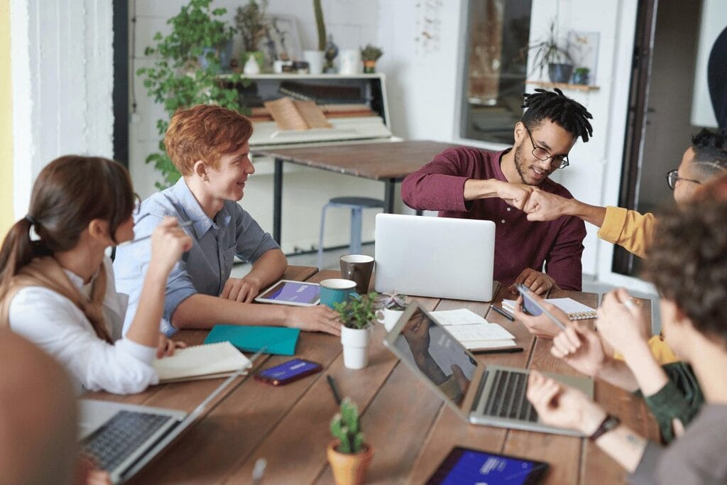 A diverse group of individuals collaborating around a table, each engaged with their laptops in a productive environment.