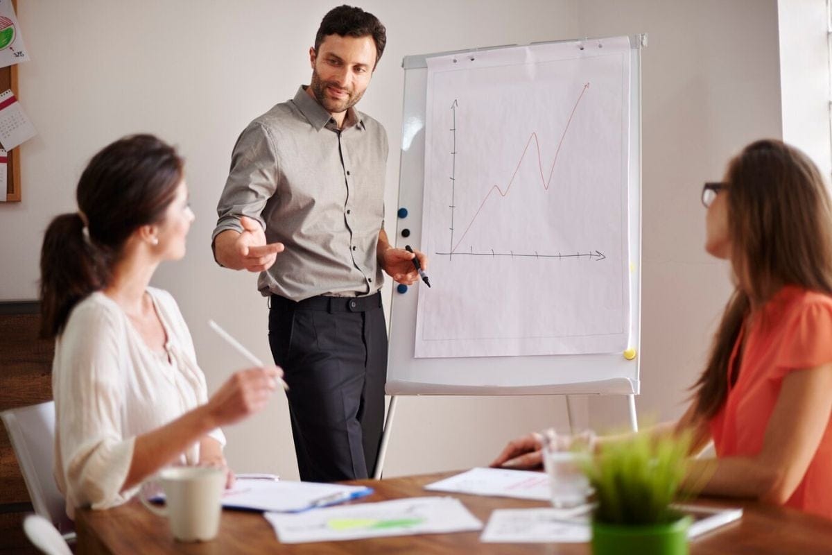 Businessman presenting a line graph to two colleagues during a meeting.
