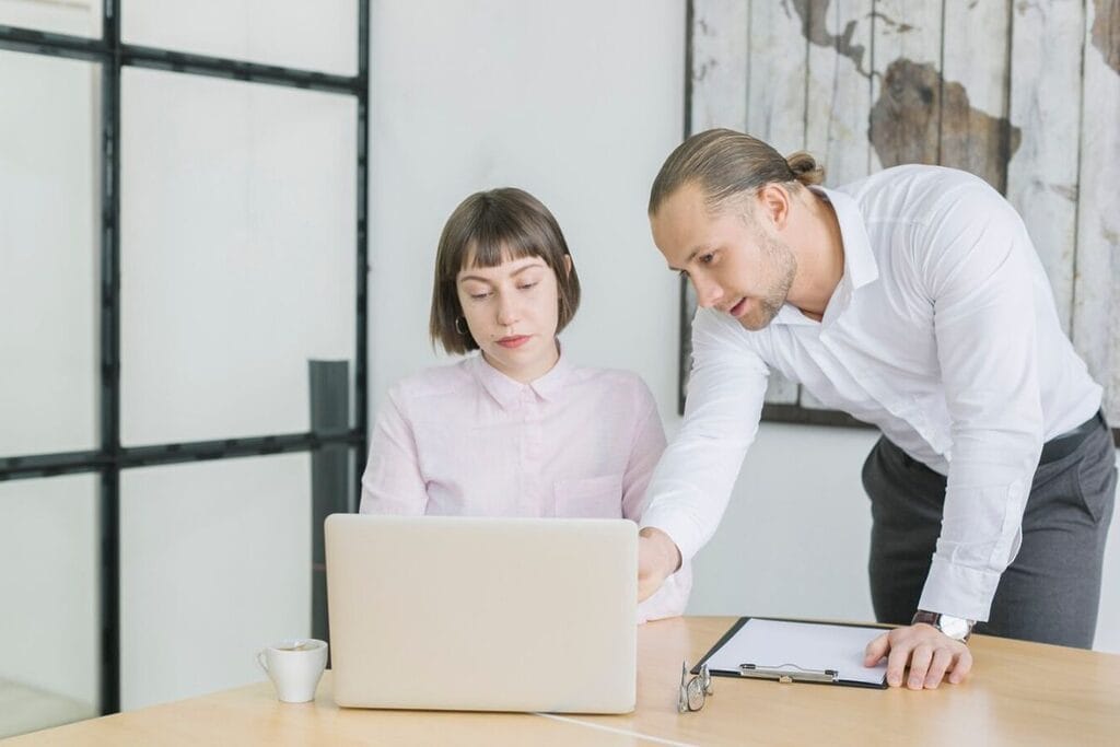 Man assisting a woman with a work task on her laptop.