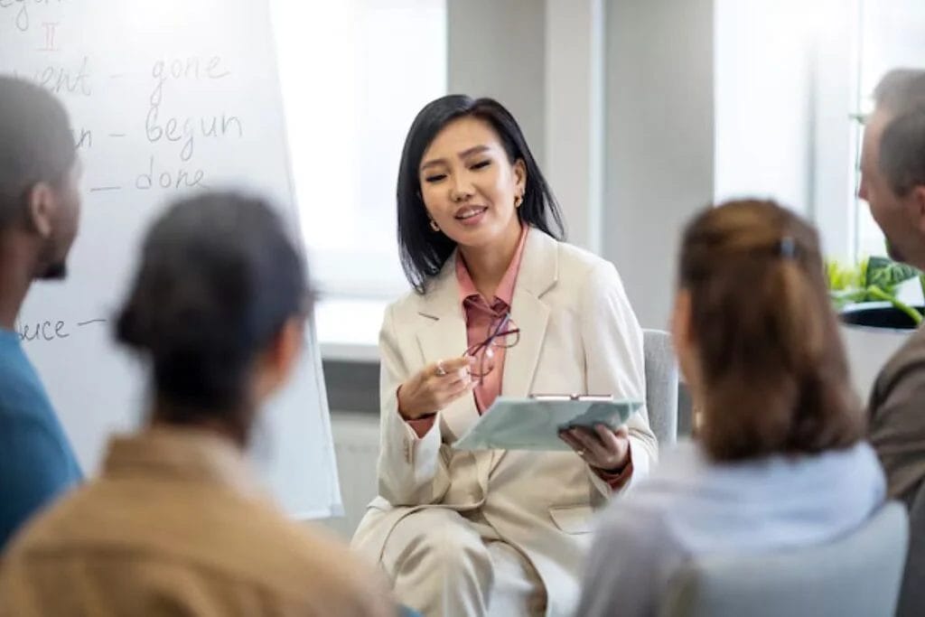 Educator teaching a small group of students, holding glasses and a clipboard during a lesson.