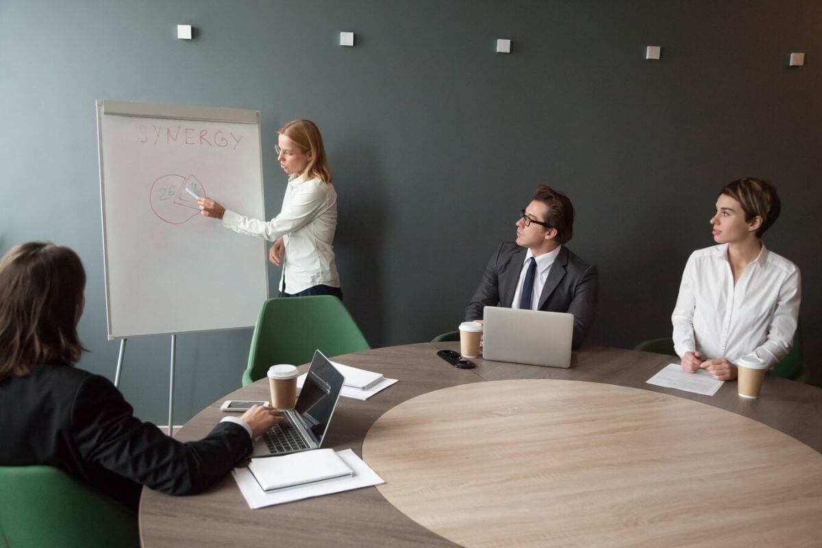 A woman confidently presents to her colleagues in a professional setting, engaging them with her insights and ideas.