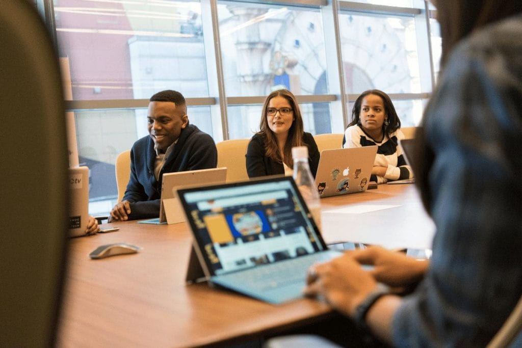 A diverse group of individuals collaborates around a table, each engaged with their laptops in a productive environment.