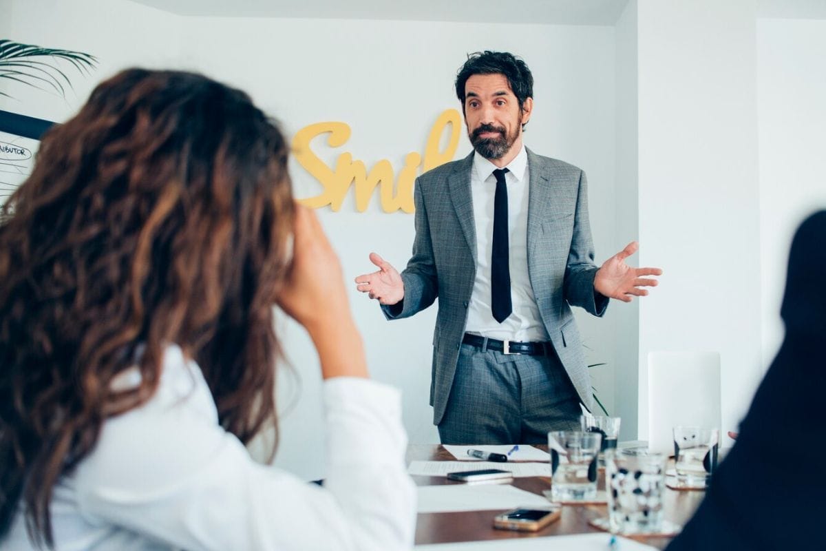 A man in a suit presents to his colleagues, engaging them with his professional demeanor and clear communication.