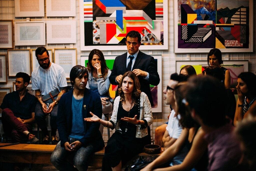 A diverse group of individuals seated in a room adorned with various pieces of art on the walls.