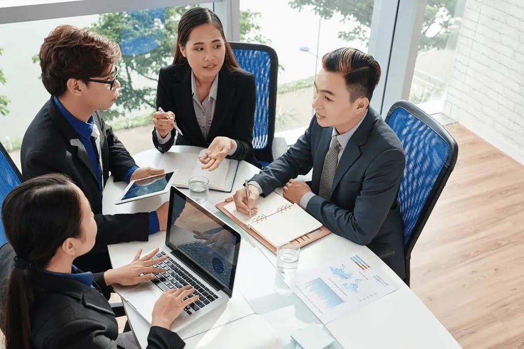 A group of young professionals collaborating around a table, with one person showing something on a tablet.