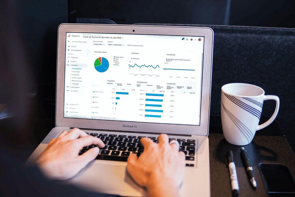 Person typing on a laptop with analytics displayed on the screen, a coffee cup on the side.