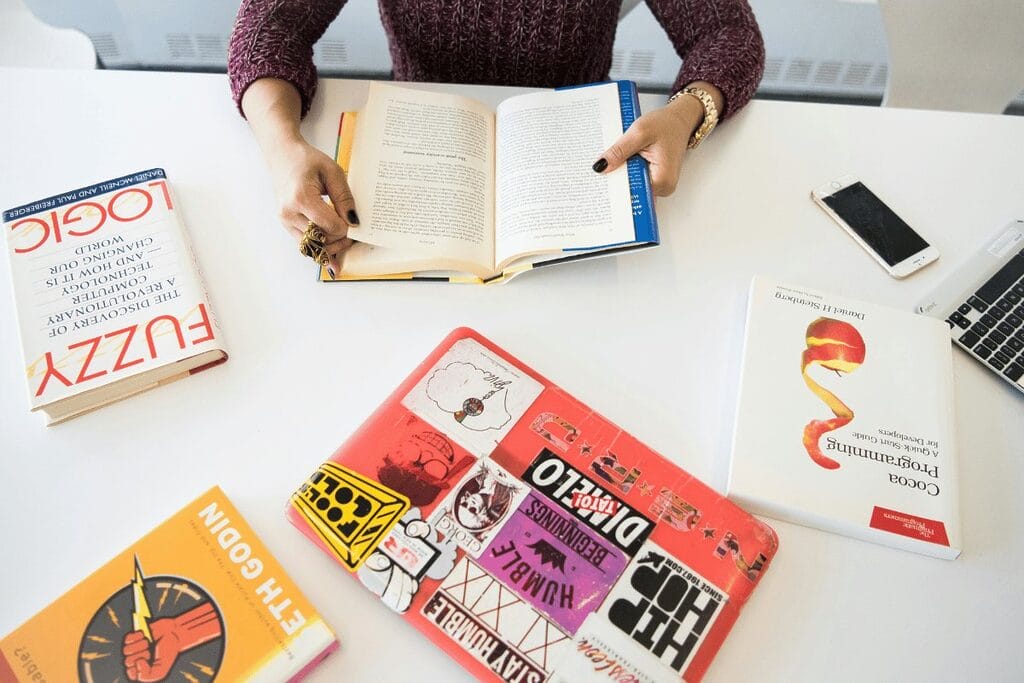 Person studying with open books and smartphone on a white table.