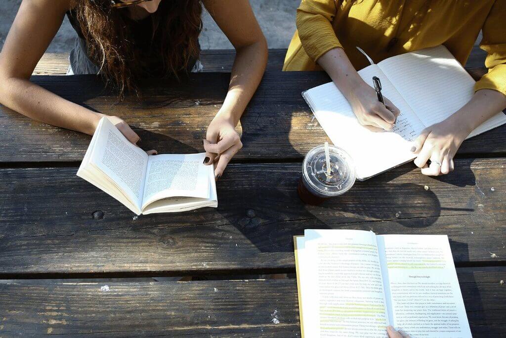 Three individuals seated at a table, engaged in reading books, surrounded by a cozy and intellectual atmosphere.