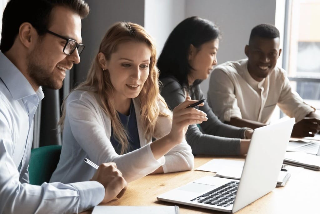Group of professionals in a meeting around a laptop on a desk.