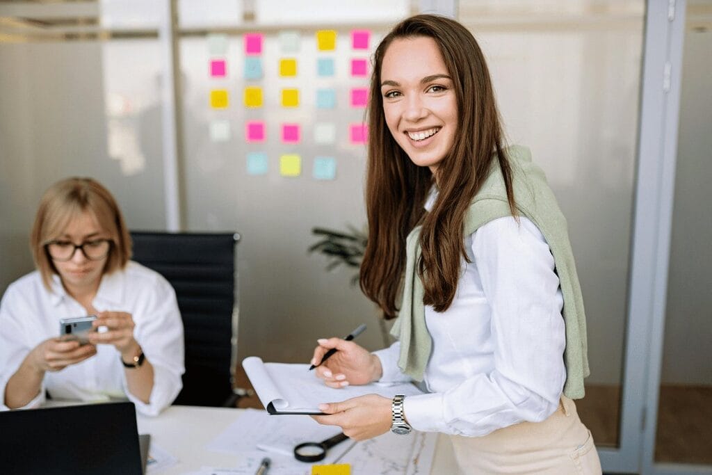 Two professionals in an office setting with sticky notes on glass and one person writing on a notepad.