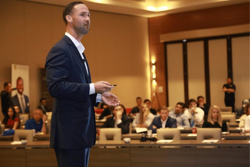 Speaker in a suit presenting to attendees at a corporate event, engaging the audience.