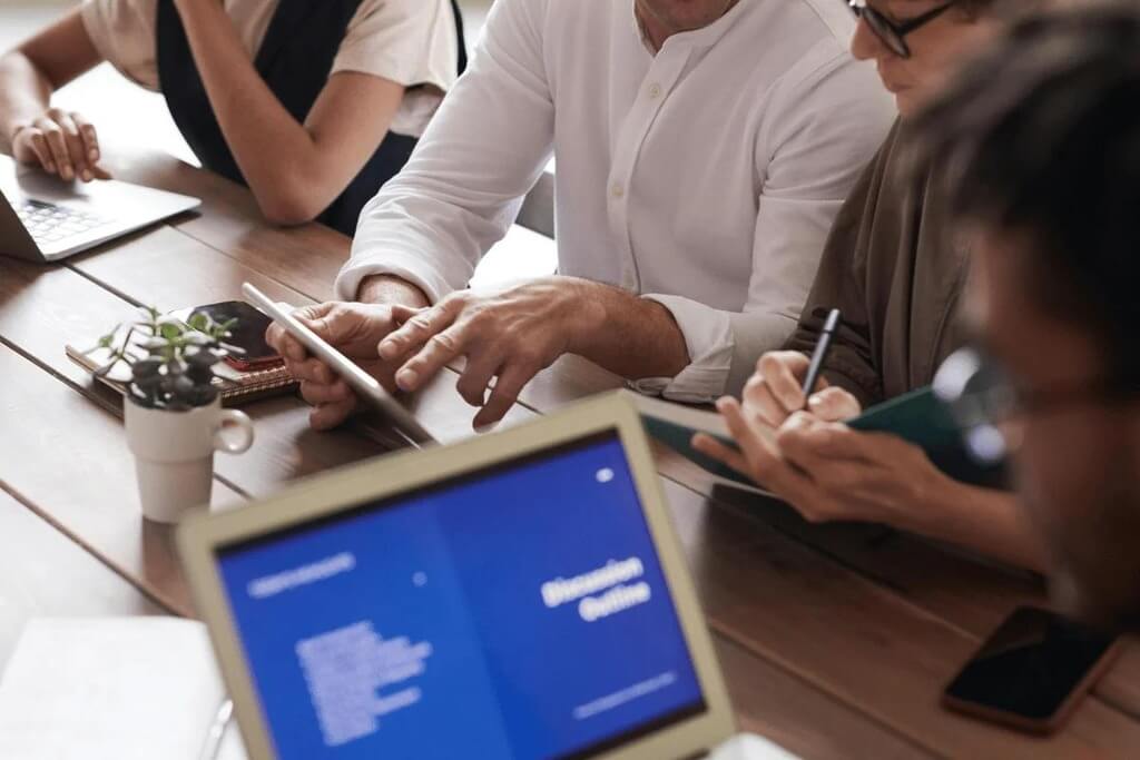 Group of professionals discussing a project around a table with laptops and tablets.