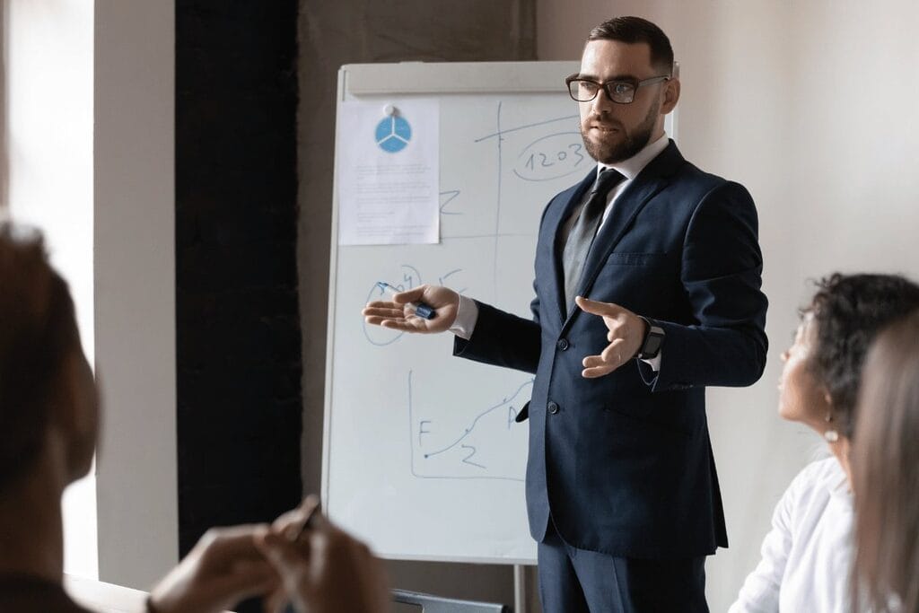 A person in a suit presenting a chart to an audience during a meeting.