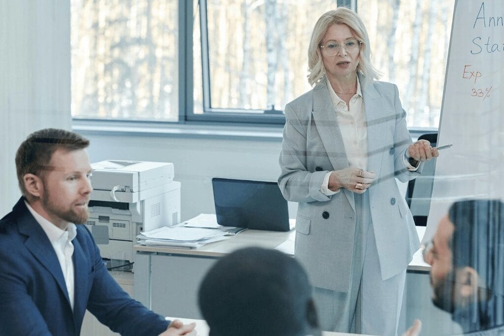 Person presenting on whiteboard during a business meeting in an office setting.