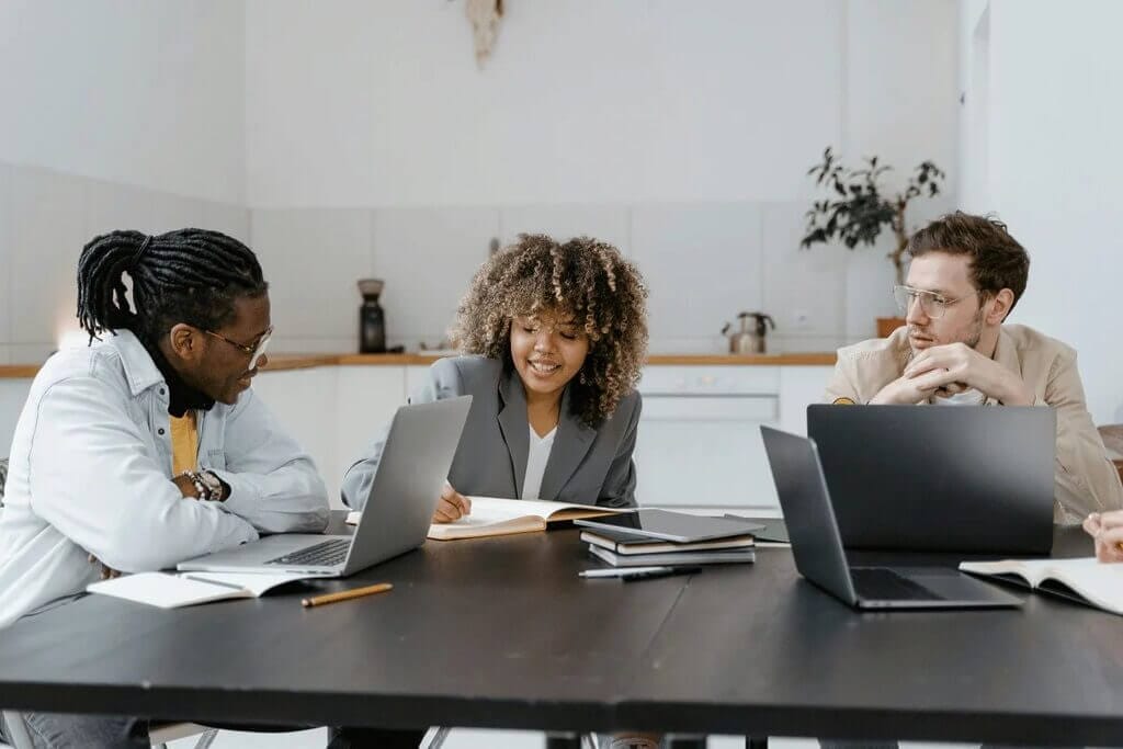 Team discussion around a table with a woman taking notes and two men listening.