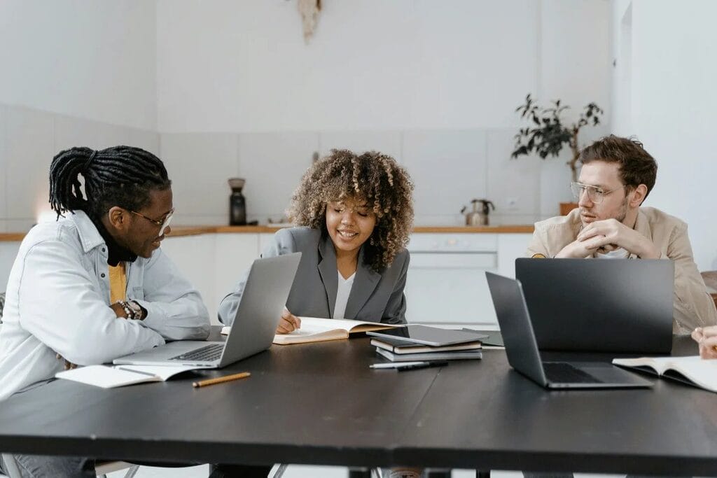 Team discussion around a table with a woman taking notes and two men listening.