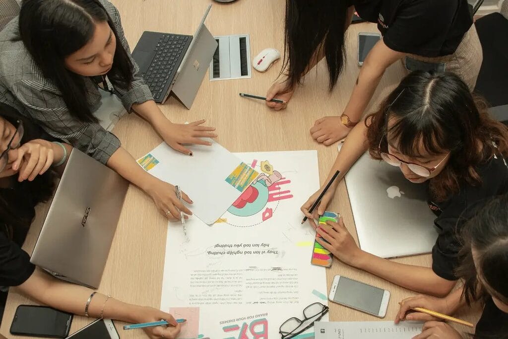 Group of people collaborating on a project around a table with laptops, papers, and phones.