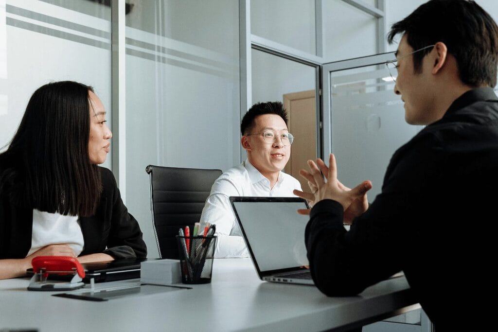 Three professionals in a meeting with a laptop on the table in an office setting.