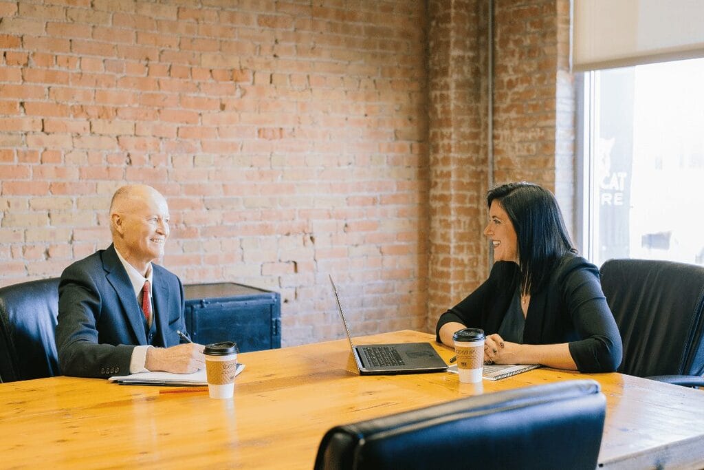Two professionals in a meeting at a table with laptop and coffee cups.