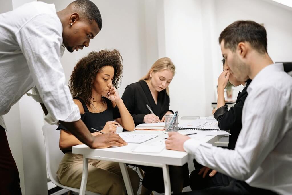 Team meeting with four focused individuals working on documents and notes in a bright workspace.